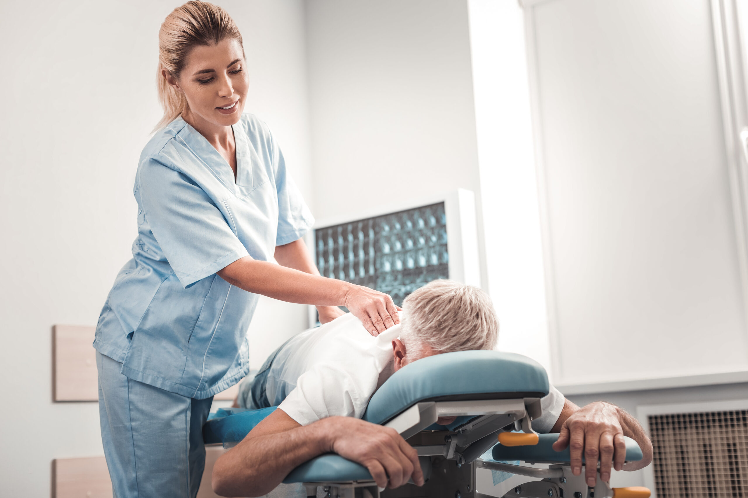 Blonde-haired chiropractor checking spine of elderly man